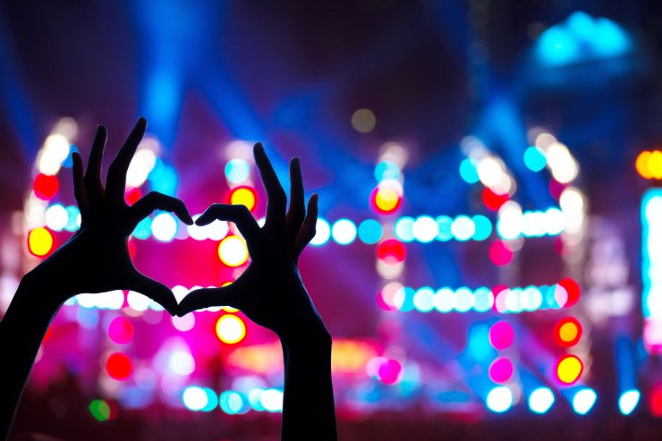 Ragazza che fa un cuore con le mani e palco di un concerto sullo sfondo