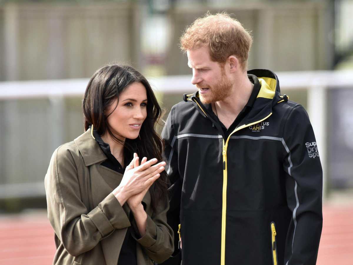 Harry e Meghan insieme, lui la guarda serio, lei a mani congiunte