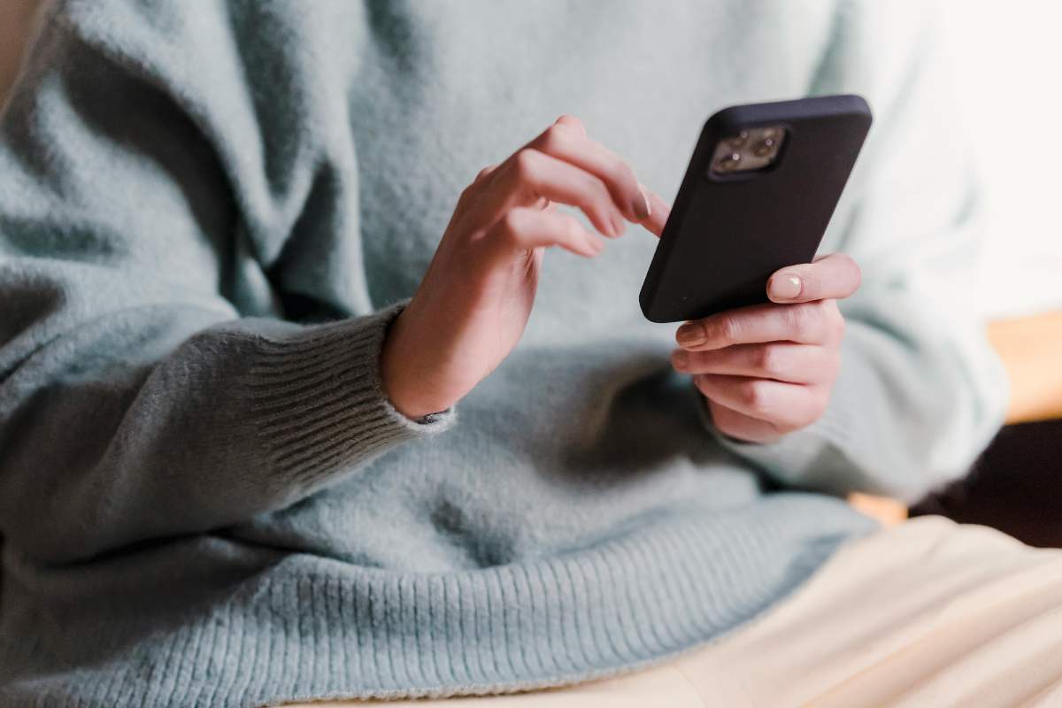Una ragazza con un maglione che risponde a un SMS sul telefono
