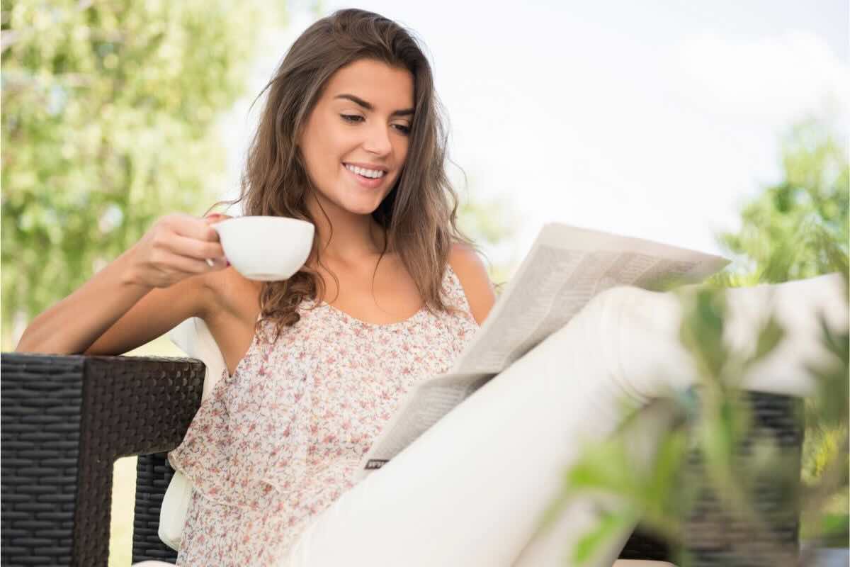 Ragazza con tazza in mano, legge giornale all'aperto