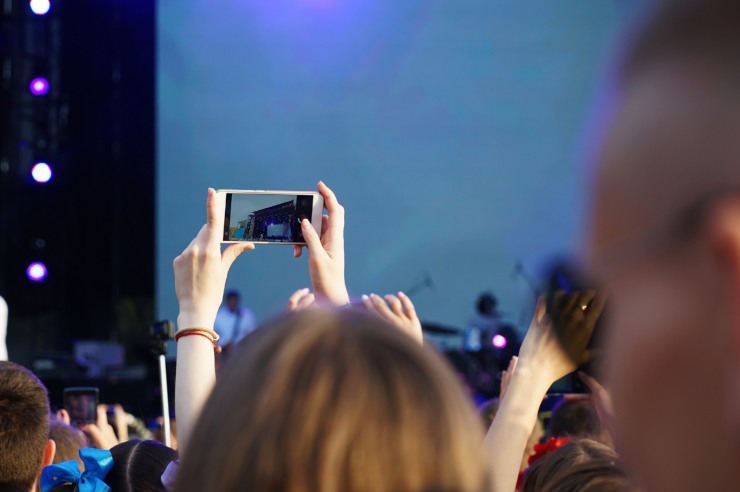Pubblico di fronte ad un palco all'aperto e ragazza che fa una foto