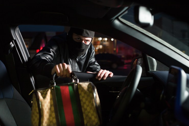 Ladro che prende una borsa dentro un'auto con finestrino aperto