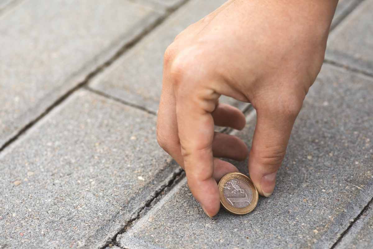 Mano che raccoglie una moneta da 1€ caduta per terra
