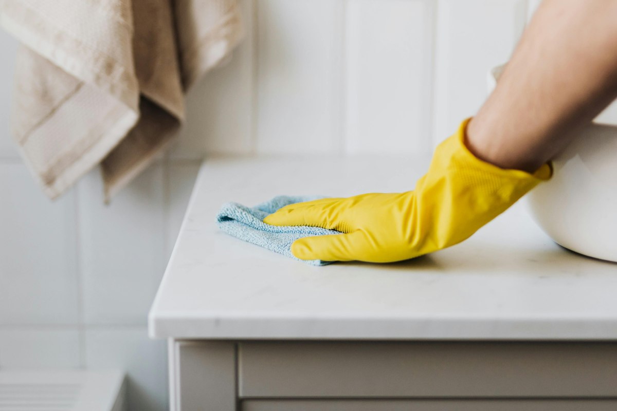 Una mano che pulisce il piano del lavandino in bagno