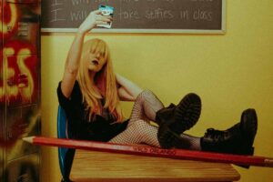 Una ragazza seduta su una cattedra di scuola che si scatta un selfie