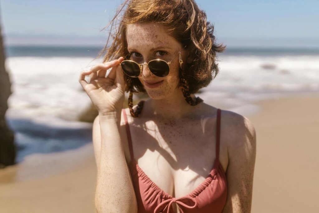 Ragazza in costume al mare che si abbassa gli occhiali da sole sul naso