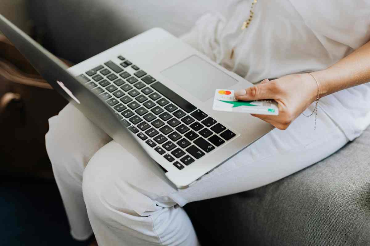 Una ragazza con un portatile sulle gambe e una carta di credito in mano