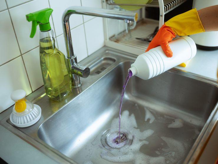 persona che versa un liquido nel lavandino per sturare lo scarico