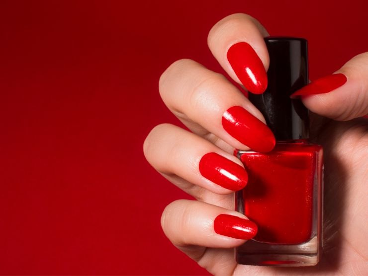 unghie con smalto rosso che mantengono una boccettina di smalto